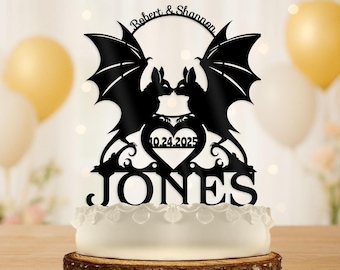 Può includere: Topper per torta nero con due sagome di pipistrelli che si baciano, con le ali spiegate. I nomi "Robert & Shannon" sono sopra, e la data "10.24.2025" è in un cuore. Il cognome "Jones" è sotto.