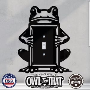 Puede incluir: Una silueta de rana negra sosteniendo una tapa de interruptor de luz negra con un interruptor de palanca blanco. La tapa está diseñada para ser personalizada con un nombre o un mensaje. La imagen incluye el texto "OWL TOP THAT" y "PERSONALISED ACRYLIC GIFTS".