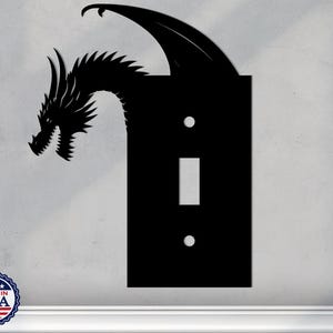 May include: Black silhouette of a dragon with wings outstretched, covering a light switch plate. The switch plate has a single toggle switch and two small circles.