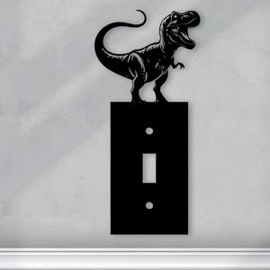 May include: Black light switch cover with a dinosaur silhouette on top. The dinosaur is facing right and has a long tail.