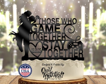 May include: Black silhouette cake topper featuring a couple holding a video game controller with the text "Those who game together stay together" and the date "03.31.25" in a heart. The topper is made in the USA.