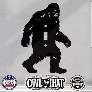 May include: Black acrylic Bigfoot light switch cover. The design features a silhouette of the legendary creature with a light switch and two screws. The cover is designed and crafted by Owl Top That, personalized acrylic gifts. Made in the USA.