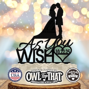 May include: Black acrylic cake topper featuring a silhouette of a bride and groom with the text "As You Wish" and a heart with the date "10.22.25". The topper is on a white cake with a brown wooden base. The cake is decorated with a red, white, and blue "Made in USA" sticker, a black and white "OWL Top THAT" sticker, and a white "Individually Made with Love" sticker.