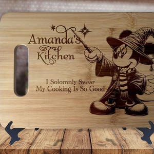 May include: A personalized bamboo cutting board with a Mickey Mouse character dressed as a wizard. The board has a handle and the text "Amanda's Kitchen I solemnly swear my cooking is so good" is engraved on the board.