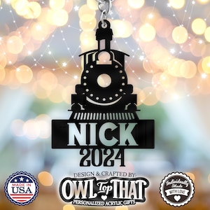 May include: Black metal train ornament with the name "NICK" and the year "2024" on it. The ornament is designed and crafted by "OWL TOP THAT" and is a personalized acrylic gift.