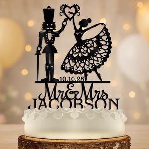 Puede incluir: Topper de pastel en silueta negra con un cascanueces y una bailarina tomándose de la mano. El topper incluye el texto "Mr & Mrs Jacobson" y la fecha "10.10.25".
