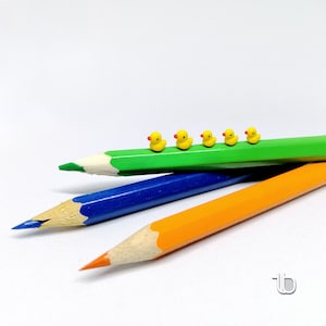 May include: Five yellow rubber duckies lined up on a green pencil, with a blue pencil and an orange pencil underneath.