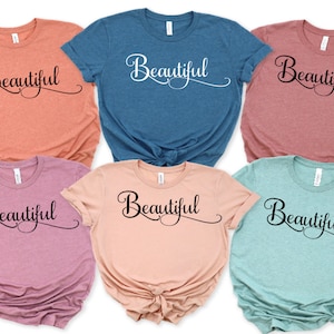 May include: Six t-shirts in different colors with the word "Beautiful" written in a cursive font on the front.