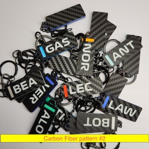 May include: A collection of carbon fiber pattern keychains with black key rings. Each keychain has a rectangular shape with white text and colored accents. The text includes words like "GAS", "NOR", and "ANT". The image also includes the text "Carbon Fiber pattern #2".