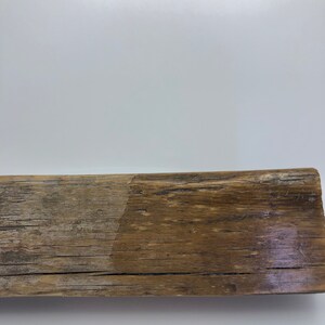 Puede incluir: Una pieza rectangular de madera envejecida, con un aspecto natural y antiguo. La madera muestra una mezcla de tonos marrones claros y oscuros, con vetas y textura visibles. La superficie es rugosa e irregular, sugiriendo exposici&oacute;n a los elementos.