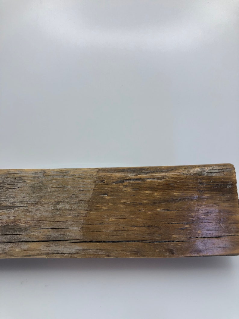 Puede incluir: Una pieza rectangular de madera envejecida, con un aspecto natural y antiguo. La madera muestra una mezcla de tonos marrones claros y oscuros, con vetas y textura visibles. La superficie es rugosa e irregular, sugiriendo exposici&oacute;n a los elementos.