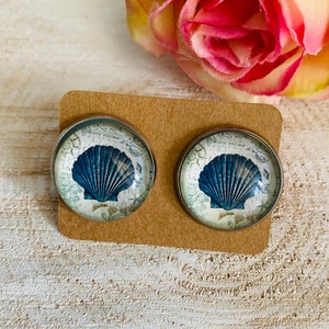 Peut inclure: Une paire de boucles d'oreilles argentées avec un motif de coquillage bleu sur fond blanc. Les boucles d'oreilles sont sur une carte marron.