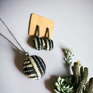 Puede incluir: Un conjunto de pendientes y collar tejidos en blanco y negro. Los pendientes y el collar presentan un diseño circular con un patrón tejido.