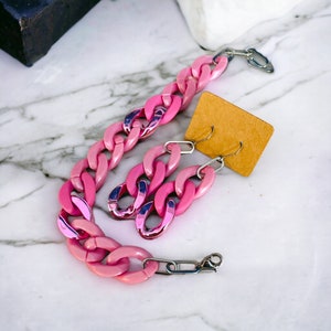 May include: A pink chunky chain necklace and matching earrings. The necklace is made of large, linked plastic pieces. The earrings are long and dangle.