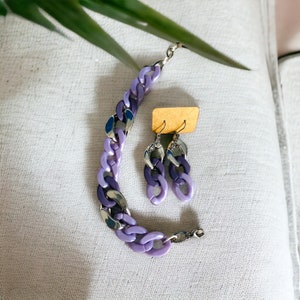May include: A matching jewelry set featuring a bracelet and earrings. The bracelet and earrings have a chain link design with alternating purple and silver links. The earrings are hanging on a small, tan cardboard tag.