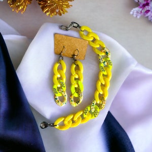 May include: A yellow chain link bracelet and matching earrings. The links are decorated with colorful flecks of paint.
