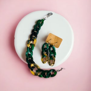 May include: A green and gold chain link necklace and matching earrings. The necklace and earrings are made of plastic and have a chunky, bold design.