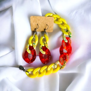 May include: A set of yellow and red chain link earrings and necklace. The earrings and necklace are made of plastic and have a speckled pattern.