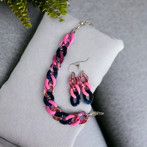 May include: A pink and blue chunky chain necklace and matching earrings. The necklace and earrings are made of plastic and have a glossy finish.
