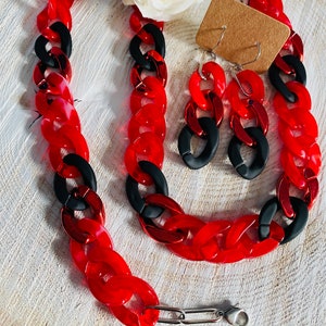 May include: A red and black chain necklace and matching earrings. The necklace and earrings are made of chunky plastic links.