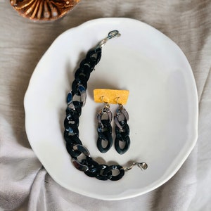 May include: A black and silver chunky chain necklace and matching earrings. The necklace and earrings are made of plastic and metal.