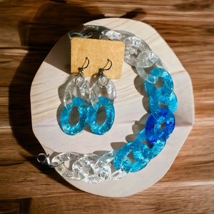May include: A set of blue and clear resin earrings and a matching bracelet. The jewelry features a chunky chain link design with glitter embedded in the resin.