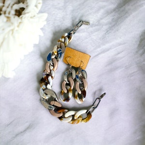 May include: A chunky chain bracelet and a pair of earrings with brown, white, and silver accents. The jewelry is made of plastic and metal.