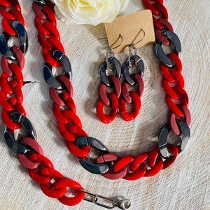 May include: A red and black chunky chain necklace and matching earrings. The necklace is made of large, interlocking links. The earrings are a similar design, but smaller.