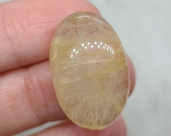 May include: A translucent oval-shaped gemstone with gold inclusions. The gemstone is light yellow in color and has a smooth, polished surface.
