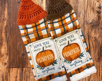 May include: Two orange and brown kitchen towels with a plaid pattern and a crocheted hanging loop. The towels feature a pumpkin design with the text "Love you more than pumpkin anything".