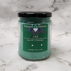 May include: A green glass candle jar with a black lid. The label reads "Kanpai Creations Ciel Tea Leaves, Lemon, and Jasmine Scented Inspired by Ciel Phantomhive Handmade With Soy Wax".