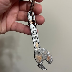 May include: A silver wrench keychain with a copper wire wrap and the word "RobCo" engraved on the handle.