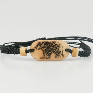 Op de afbeelding: Zwart gevlochten armband met een ovale houten bedel met een gedetailleerd zwart-wit berenontwerp.