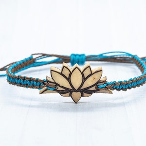 May include: A brown and blue braided bracelet with a wooden lotus flower charm. The charm is light brown with a dark brown outline.