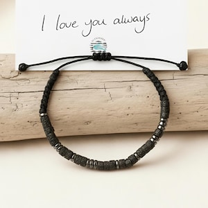 May include: Black beaded bracelet with a Morse code message. The card above the bracelet reads "YOUR MORSE CODE MESSAGE SAYS I love you always". The bracelet features dark gray cylindrical beads and silver-colored metal beads.