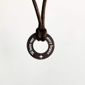 May include: A brown leather cord necklace with a circular pendant that reads "Where our story began".