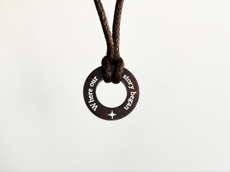 May include: A brown leather cord necklace with a circular pendant that reads "Where our story began".