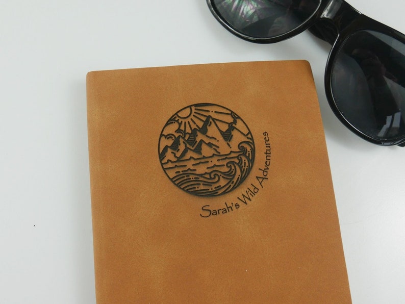 A brown, personalized journal. The cover is engraved with a unique travel design, along with your name and the phrase “wild adventures”.