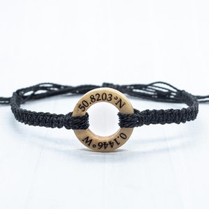 May include: Black braided bracelet with a wooden circle charm engraved with the coordinates "50.8203&deg;N 0.1446&deg;W".