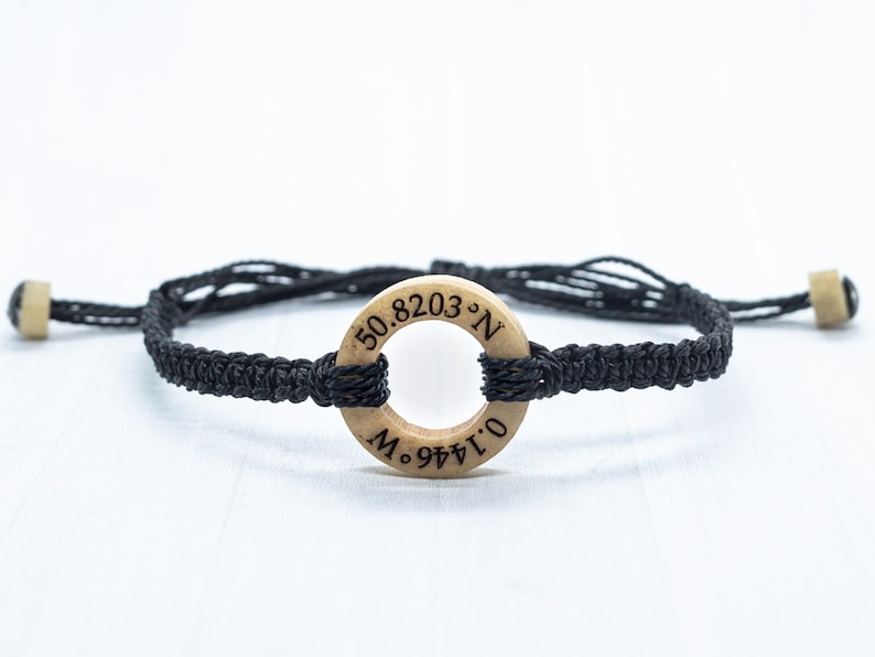 May include: Black braided bracelet with a wooden circle charm engraved with the coordinates "50.8203&deg;N 0.1446&deg;W".