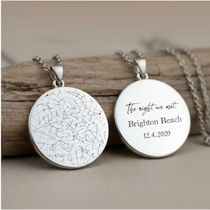 Può includere: Due collane con pendenti rotondi color argento. Un pendente mostra un disegno della mappa stellare, l'altro presenta l'iscrizione "The night we met. Brighton Beach 12.4.2020". Entrambi i pendenti hanno catene delicate.