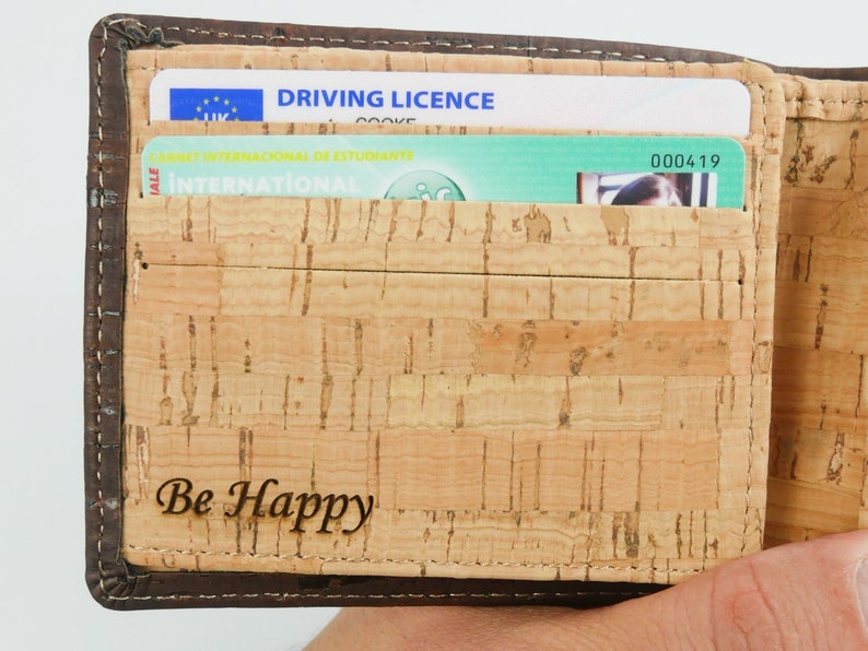 Inside of personalised cork wallet is  engraved "Be happy". Open wallet displaying card slots holding cards.