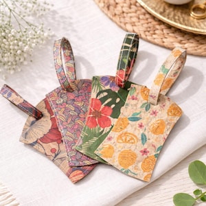 Op de afbeelding: Vier decoratieve bagagelabels met kleurrijke bloemen- en fruitpatronen. De labels hebben een kurkachtige textuur en zijn voorzien van ontwerpen in rode, roze, groene en gele tinten. Elk label heeft een bijpassende lus voor bevestiging.