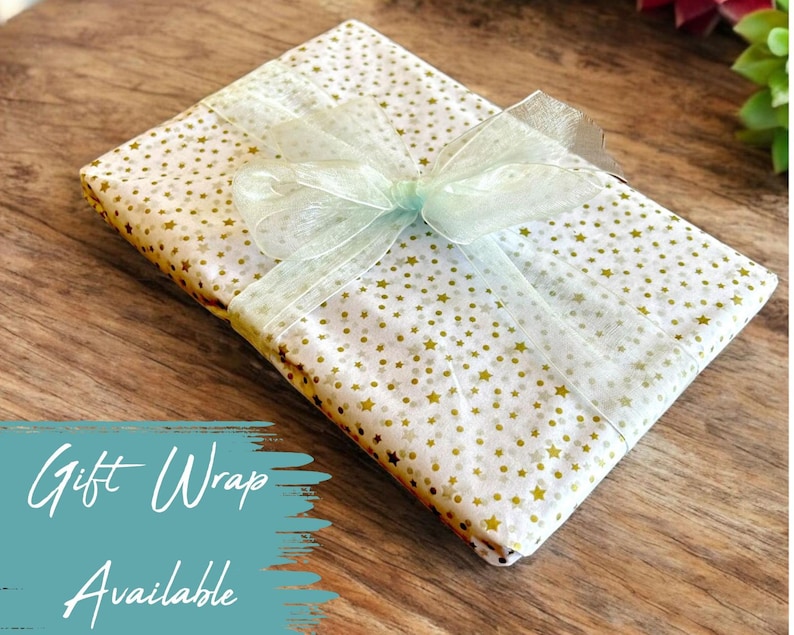 May include: A white gift box with a gold star pattern is wrapped with a light green ribbon. The box is sitting on a wooden surface.