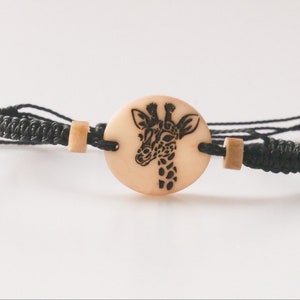 Puede incluir: Pulsera trenzada negra con un dije de madera con un diseño de jirafa en blanco y negro.