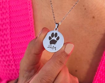 May include: A silver necklace with a round pendant featuring a black paw print and the name "Shelly" engraved on it.