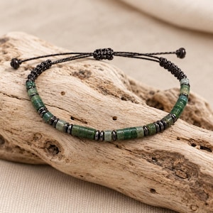 May include: A bracelet featuring alternating cylindrical green stone beads and small metallic dark gray spacer beads. The piece is strung on a thin black cord with a sliding knot closure, finished with two small black knots at the ends.