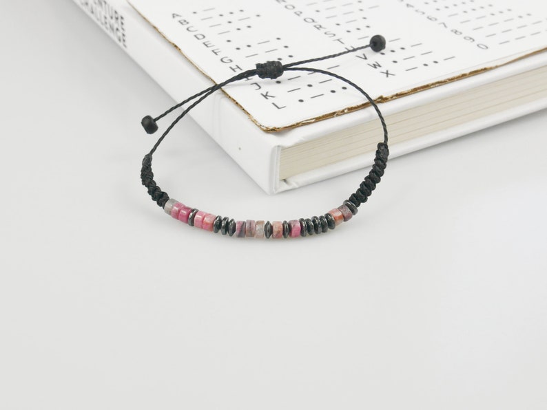 Pink Jade and Hematite beaded Morse code bracelet with waxed cotton cord, photographed on hardback book with Morse code example sheet.