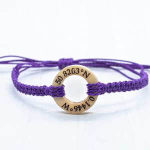 May include: Purple braided bracelet with a wooden circle charm engraved with the coordinates "50.8203&deg; N 0.1446&deg; E".