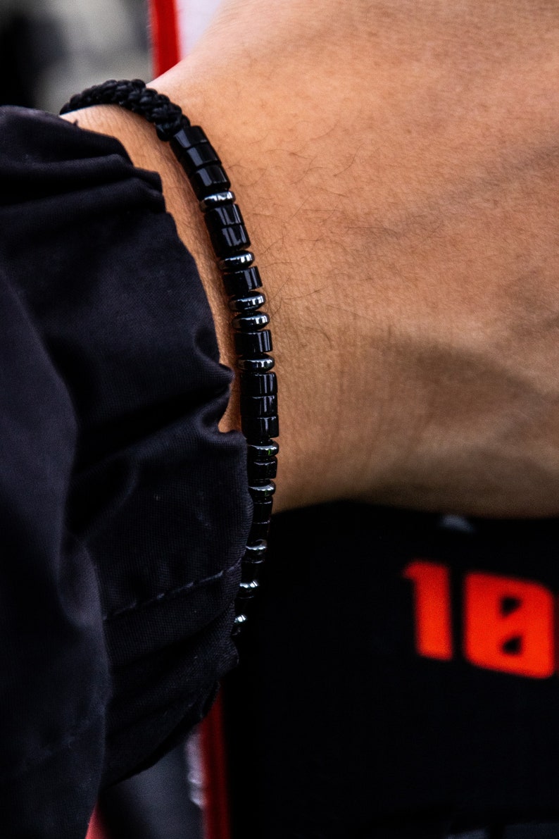 May include: A black beaded bracelet with silver accents. The bracelet is made of small, round beads that are strung together on a black cord.